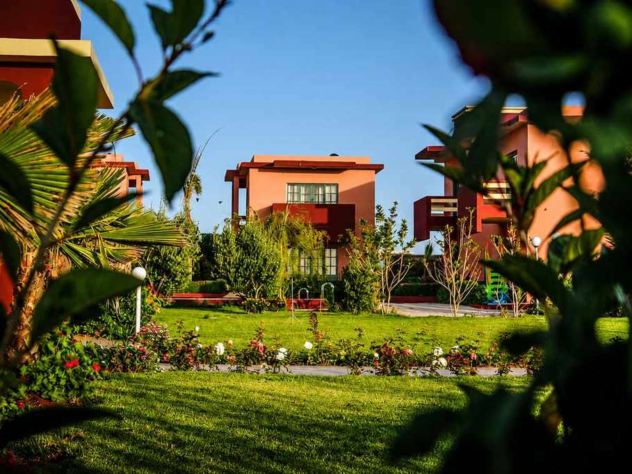 Rose garden with palms and terracotta villas at Hotel Zerad in golden evening light